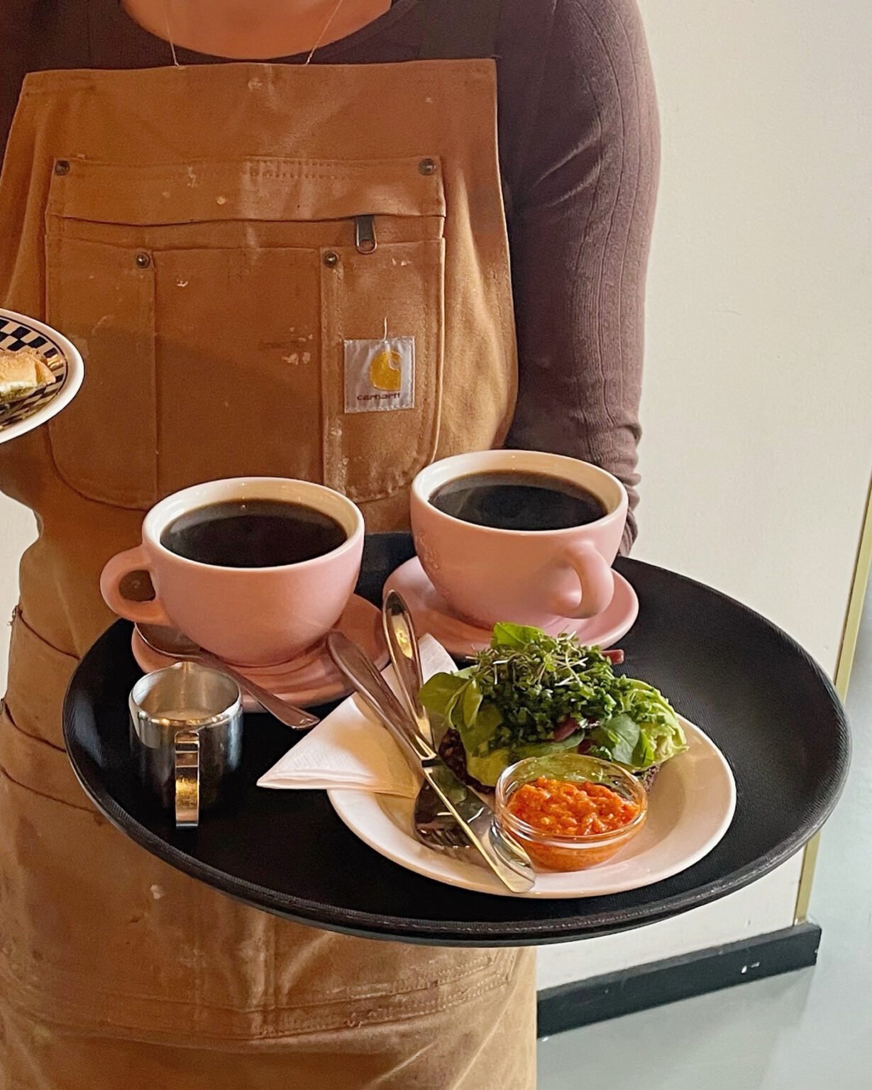 Barista hos Stillestund serverer kaffe og mad på en bakke